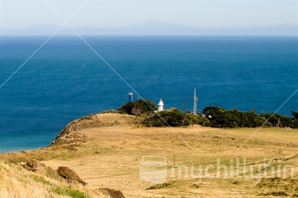 A view across the golden grass of Baring Head Regional Park, Wellington with the Baring Head light house on the middle ground and Cook Strait and the South Island in the distance