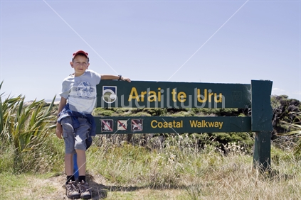 Male child sitting by the sign for the Arai te Uru walkway, Hokianga