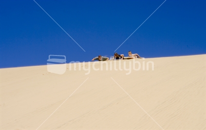 Father and children sliding down sand dune on a body board, Hokianga