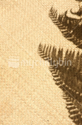 Silhouette of a fern, on a flax mat
