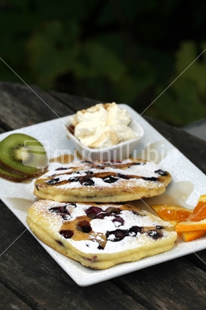 New Zealand blueberry pancakes with cream, kiwifruit and orange. 

