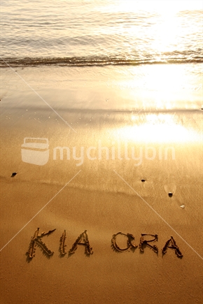 Kia Ora written in the sand at sunset
