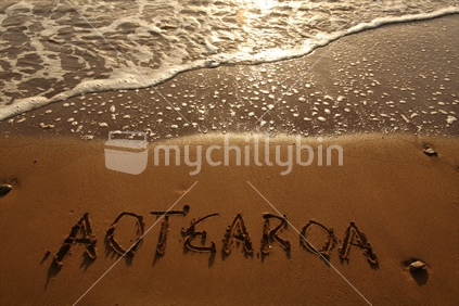 Aotearoa written in the sand at sunset
