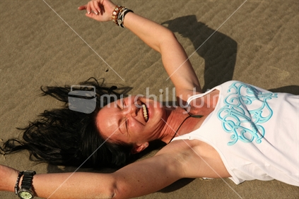 Woman enjoying the sun at Mangawhai Heads beach, Northland, New Zealand.