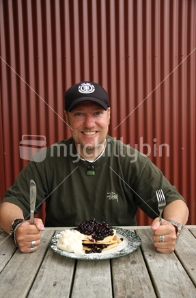 Man about to tackle a New Zealand blueberry pancakes and whipped cream snack, at outdoor cafe table. Enjoy!
