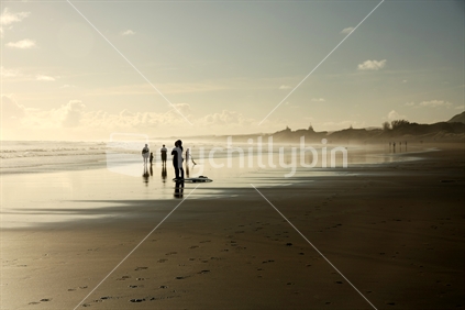 Surfers at Muriwai beach in the late afternoon sun, Auckland, New Zealand.

