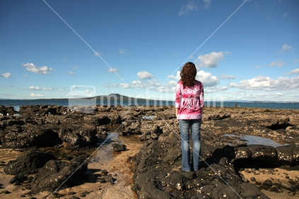 young woman admiring Takapuna's volcanic coastline with Rangitoto Island