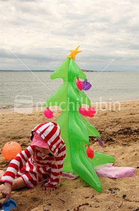 Girl is enjoying the christmas holidays on the beach - with an inflatable christmas tree. 
