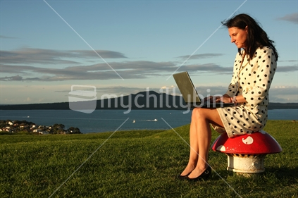 Woman sitting on the mushroom at Mt Victoria with a laptop and Rangitoto Island in the background, Devonport, Auckland

