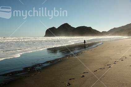 Person walking along Bethells Beach on a clear winter day, Waitakeres, Auckland