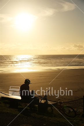 Biker at Muriwai beach in the late afternoon sun, Auckland, New Zealand.