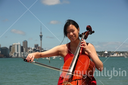 Woman playing a cello in front of the Auckland skyline, Bayswater