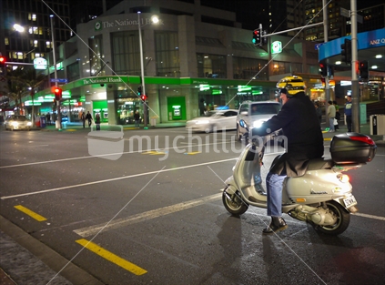Scooter rider waiting at an Auckland City intersection at night. 