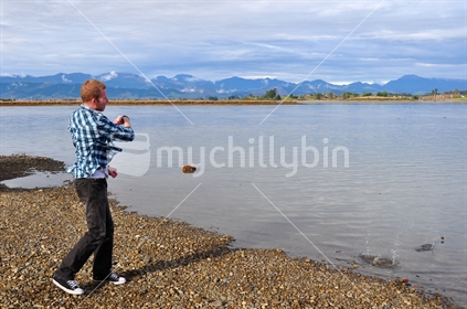Young man skimming pebbles in estuary