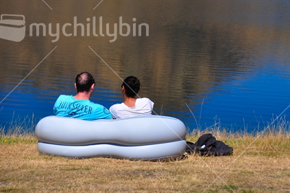 couple relaxing on lakeside in blow up sofa