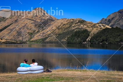 Couple sitting in blow up chair on the edge of Moke Lake, Queenstown.