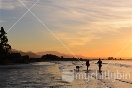 Couple and dog walking along a Nelson beach at sunset