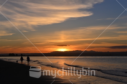 Couple walking along a Nelson beach at sunset