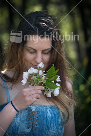 Young New Zealand woman with eyes closed smelling spring blossom, and imagining ...