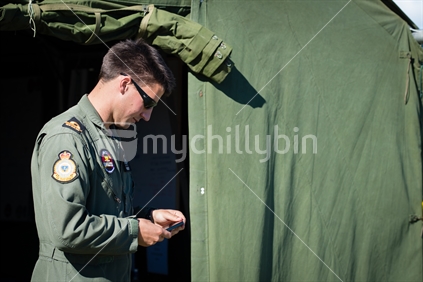 Young RNZAF pilot using cellphone beside tent at Airforce training Camp in Nelson