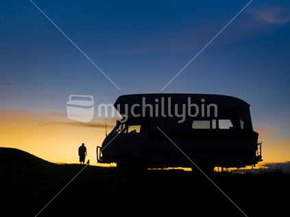 silhouetted distant man and dog watching sunset while camping in paddock overlooking the ocean on Christmas day