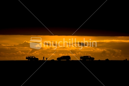Silhouette of vehicles and surfers with dark cloud above