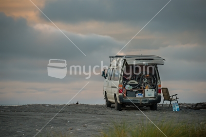 Campervan freedom camping on beach beside the ocean on westcoast beach at sunset