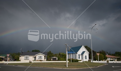 Homes and Presbyterian Church spanned by rainbow on a moody day.