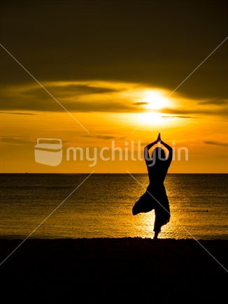 Young Woman doing Yoga on the beach at sunset