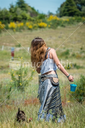 Beautufil young woman with food bucket being followed by chicken at animal farm in tasman