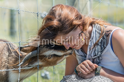 Beautiful young woman interacting with rescued wild goat through fence at  animal farm in Tasman