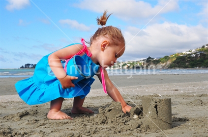 Girl playing on beach with bucket and sand castle.