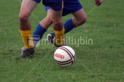 Soccer player dribbling ball with opponent tackling