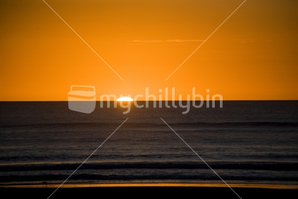 Sun setting with an orange glow over Piha beach