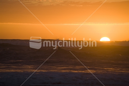 Orange sunset behind the waves at Piha beach