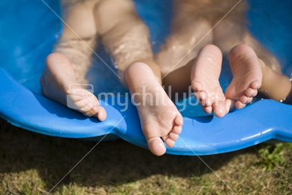 2 young kids splashing in a paddling pool in the summer sun