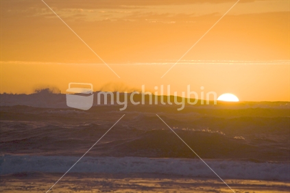 Orange sunset behind the crashing waves at Piha beach
 