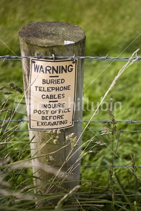 Telephone cable warning on a fence post