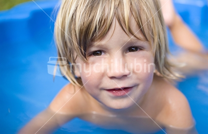 A young boy cooling off in a blue paddling pool in the summer sun