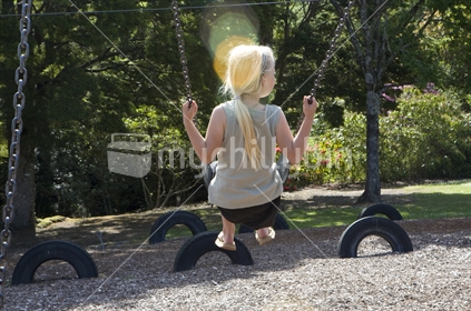 A young blonde girl swinging in late afternoon sun, with a sun spot
