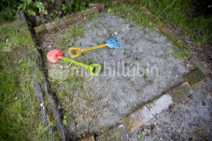 Coloured plastic spades in an overgrown sandpit