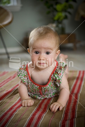 A cute little baby girl with an inquisitive look lying on a striped mat