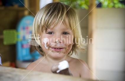 Young blonde boy enjoying a summer ice cream whilst getting it all over himself