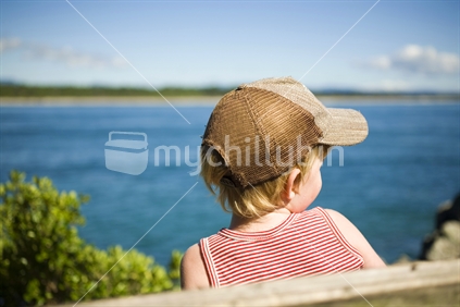 A young boy wearing a cap looking out to sea at Mount Maunganui, New Zealand