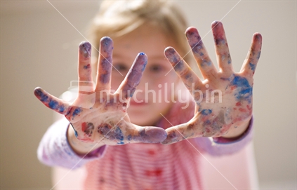 A young girls outstretched hands covered in paint