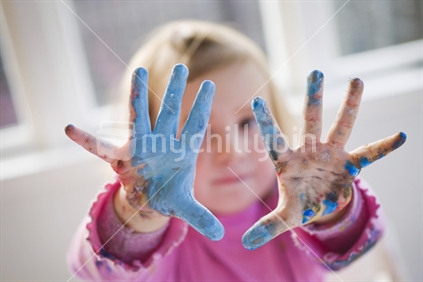 A young girls outstretched hands covered in paint