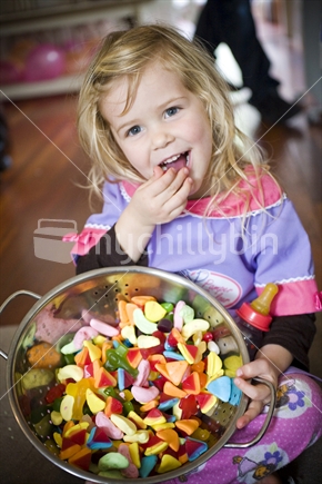 A young girl eating a large colourful bowl of lollies