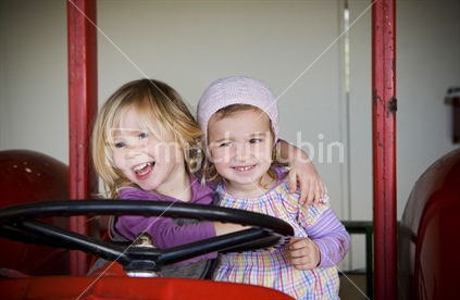Two young girls playing on a red farm tractor