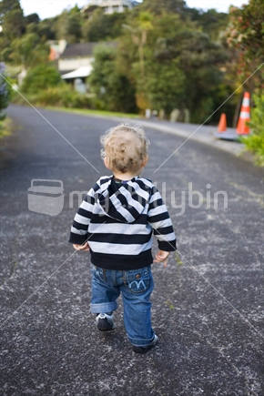 A blonde toddler in a striped top walking up a suburban walkway