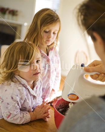 Two young girls in their pyjamas watching their mum baking